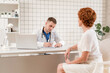 © malkovkosta - General Practitioner. Male physician and female patient. Patient Having Consultation With male Doctor In Office