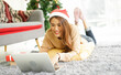 © chinnarach - close up young asian woman lay on floor to using laptop to search promotion on Black Friday or cyber Monday at living room with decorated Christmas tree for holiday lifestyle and simple life concept