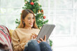 © chinnarach - close up young asian woman hold digital tablet and use social media network application or surf the internet while sitting on couch in living room for christmas holiday lifestyle concept