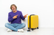 © luismolinero - Young blonde man with suitcase sitting on the floor surprised and pointing side