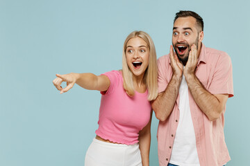 Wall Mural - Young couple two friends family surprised man woman in casual clothes point finger aside on workspace together isolated on pastel plain light blue background studio portrait People lifestyle concept.