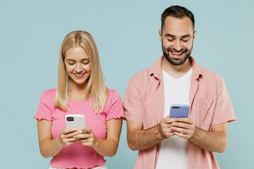 Young couple two friends family man woman in casual clothes hold in hand use mobile cell phone together isolated on pastel plain light blue color background studio portrait People lifestyle concept.