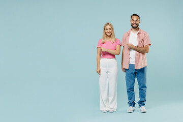 Wall Mural - Full body young cool couple two friends family man woman in casual clothes point index finger aside on workspace area mock up copy space together isolated on pastel plain light blue background studio.