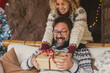 © simona - Christmas eve holidays gif exchange activity with man and woman at home. Female give present at adult male sitting on the sofa. Lady make a surprise tu her husband with box
