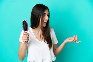 Canvas Print - Young caucasian woman with hair comb isolated on blue background with surprise facial expression