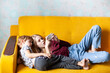 © Natallia - Children laying on the yellow sofa playing online games on smartphone or surfing a net. Modern communication, online studying, internet addiction concept. Selective focus.