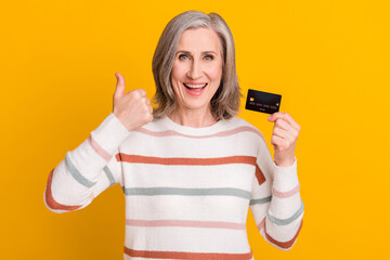 Sticker - Photo of adorable shiny retired woman dressed white sweater holding debit card showing thumb up isolated yellow color background