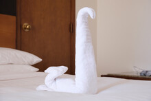 Folded From A White Towel Swan On The Bed In The Hotel Room. Traditional Decoration Of The Rooms Of The Hotel Guests When Cleaning The Rooms.