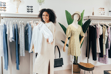 Wall Mural - Cheerful woman trying on a shirt while standing at a rack in a small boutique