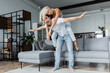 © LIGHTFIELD STUDIOS - happy man with outstretched hands piggybacking blonde girlfriend in living room