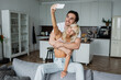 © LIGHTFIELD STUDIOS - happy woman taking selfie with cheerful boyfriend in living room