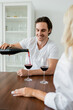 © LIGHTFIELD STUDIOS - cheerful man pouring red wine into glass near blurred girlfriend