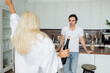 © LIGHTFIELD STUDIOS - tattooed man looking at blurred blonde woman with bottle of wine in kitchen