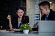 © David - Business people working together. Serious businessman with laptop talking to a businesswoman with papers and tablet. Business partners have a successful meeting in the modern office.