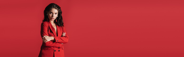 Wall Mural - young brunette model in suit posing with crossed arms isolated on red, banner.