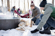 Grandfather And Grandson Chopping Firewood At Campfire In Snowy Woods