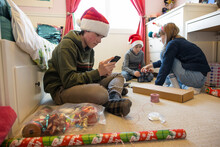 Brothers And Sister In Santa Hats Wrapping Christmas Gifts In Bedroom