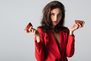 Wall Mural - young woman in trendy suit holding red pomegranate halves isolated on grey.