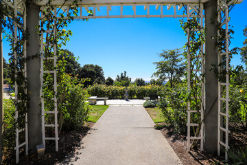 a white wooden awning in the garden covered with lush green plants and colorful flowers with a walk way leading to white flowers in the garden with blue sky at Huntington Library and Botanical Garden