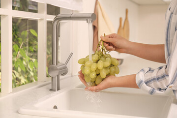 Canvas Print - Woman washing grapes under tap water in kitchen sink, closeup