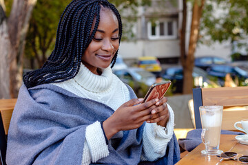 Beautiful young black girl relaxing in a coffee shop chatting and texting on social networks on her cell phone. Leisure time, technology, and urban lifestyle.	