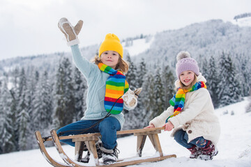 Wall Mural - Children enjoying winter, playing with sleigh ride in the winter forest. Kids play with snow. Winter vacation concept. Kids playing in the winter forest.