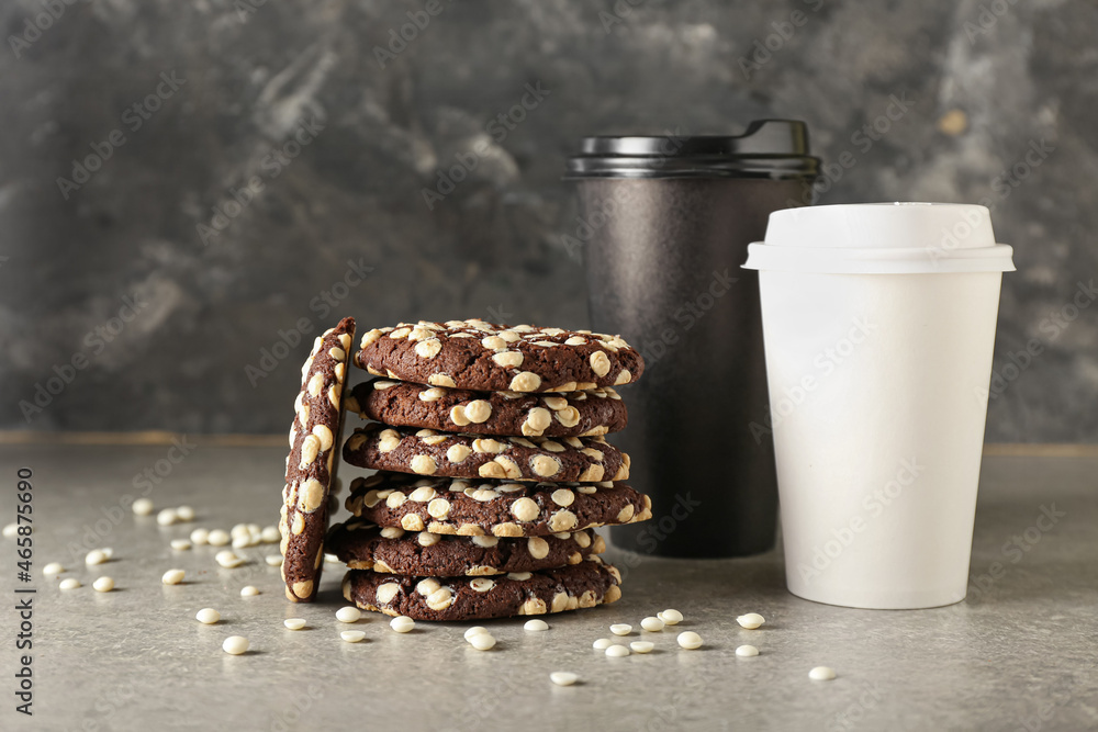 Tasty cookies with white chocolate chips and takeaway cups on table