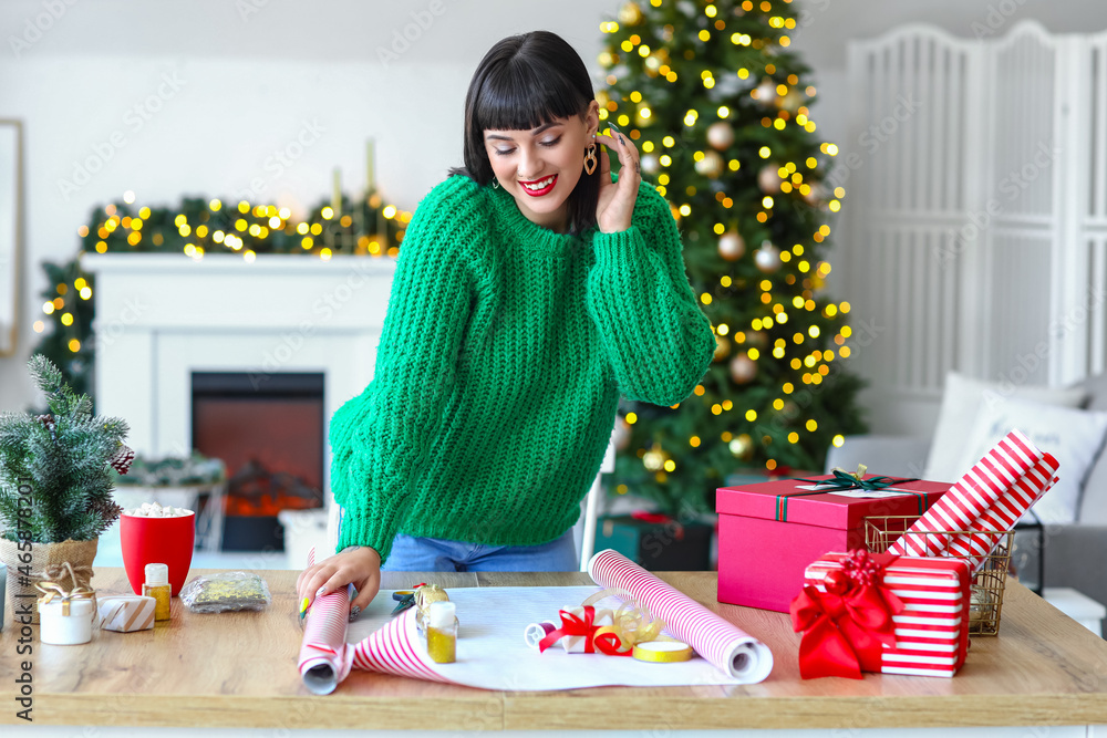 Beautiful young woman wrapping Christmas gift at home