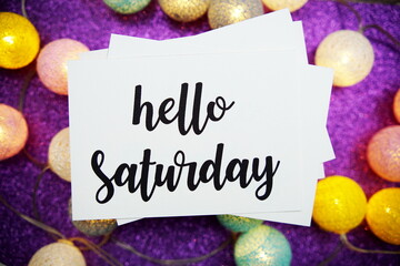 Wall Mural - hello saturday text on paper card top view on purple bokeh background