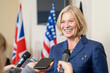 Smiling mature female politician with blond hair talking to press after summit while journalists reaching microphones