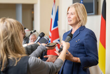 Confident Blond-haired Congresswoman Gesturing Hands While Answering Questions Of Journalists With Microphones