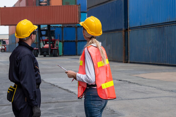 Industrial worker works with co-worker at overseas shipping container yard . Logistics supply chain management and international goods export concept .