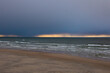 Winter or late autumn on Baltic Sea Curonian spit beach. Sand, dark blue sea and dramatic cloudy sky with a line of sunset lights. No people around, sad and depressive mood