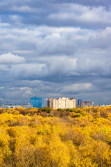 Wall Mural - dark gray rainy clouds in blue sky over lush yellow forest and modern high-rise apartment houses illuminated by sun on autumn day before rain