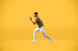 Young african american man running over yellow studio background, in motion side view shot of guy jumping in air