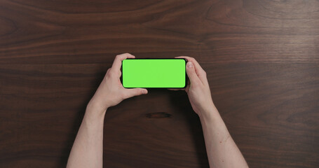 Sticker - Top view man hand hold smartphone with green screen over black walnut wood table