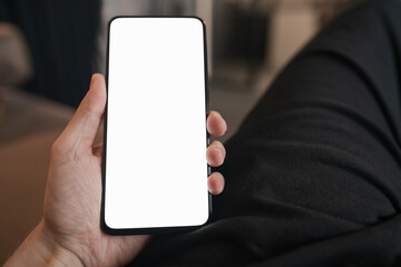 Wall Mural - Man hold smartphone with white screen in his hand sitting on a couch in home environment