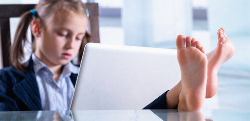 Wall Mural - Humorous photo of happy child business girl is resting and working at the same time. Selective focus on bare feet. Horizontal image.