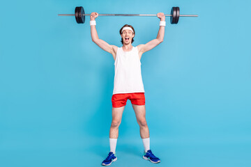 Full length photo of cool young brunet guy hold barbell wear singlet shorts sneakers socks isolated on blue background