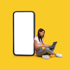 Wall Mural - smiling woman using laptop, leaning on white empty phone screen