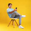 © Prostock-studio - Happy guy using mobile phone at studio, sitting on chair