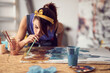 Close-up of a young female artist using a straw while working on a new painting in the studio. Art, painting, studio