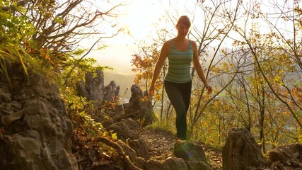 Wall Mural - SLOW MOTION, CLOSE UP, LENS FLARE: Golden autumn evening sunbeams shine on young woman hiking uphill while exploring the woods in Slovenia. Fit female hiker explores the woods on a sunny morning.