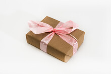 Gift Wrapped In Brown Paper And Tied With A Pink Ribbon On A White Background. Isolated