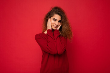 Wall Mural - Young beautiful self-confident curly brunette woman with sincere emotions poising isolated on background wall with copy space wearing casual dark red sweater. Positive concept