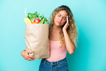 Wall Mural - Girl with curly hair holding a grocery shopping bag isolated on green background with headache