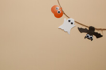 A Homemade Garland On A Jute Rope Made Of A Pumpkin, A Bat And A Ghost With Eyes In The Corner Of The Frame On A Beige Background With A Place For Text