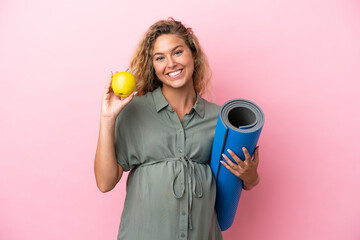 Wall Mural - Girl with curly hair isolated on pink background pregnant holding an apple and going to yoga classes