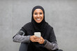 Happy Young Muslim Woman In Sportswear Relaxing With Smartphone After Outdoor Training