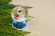 © Яна Скиданенко - A snow ball toy with a white Christmas bear and a baby on a blue stand on a beige background with green thuja branches and a place for text
